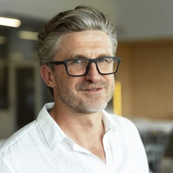 Portrait of confident smiling gray haired businessman, manager, CEO wearing stylish eyeglasses looking at camera standing in modern office. Successful business concept