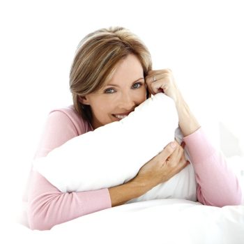 Portrait of a mature Caucasian woman hiding behind a pillow on bed