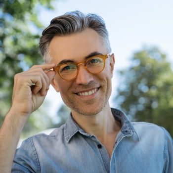 Portrait of handsome mature businessman wearing eyeglasses, standing on the street, looking at camera, smiling