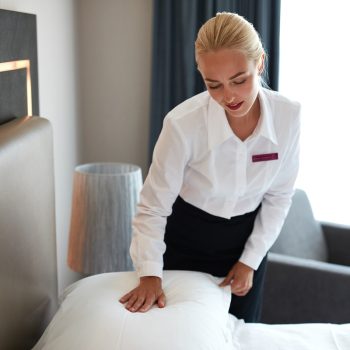 beautiful housemaid changes the pillowcase on the bed, caucasian blonde female in uniform prepares room for guests